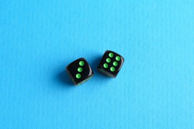 Two black game dices on light blue background, flat lay