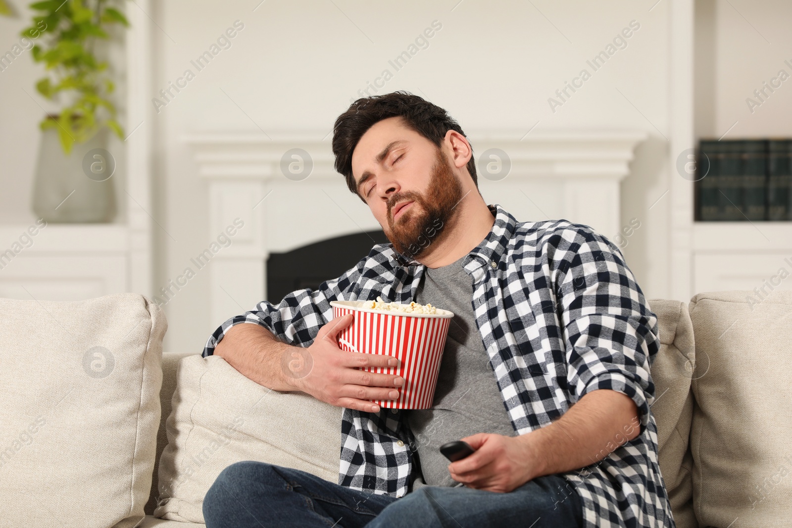 Photo of Man sleeping while watching TV with popcorn on sofa indoors