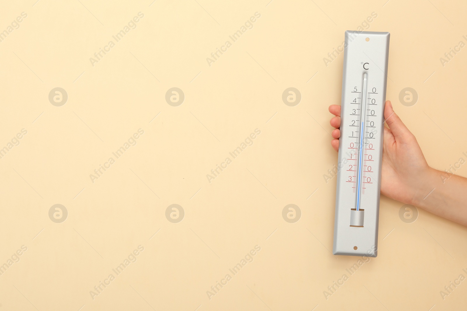 Photo of Woman with weather thermometer on beige background, closeup. Space for text