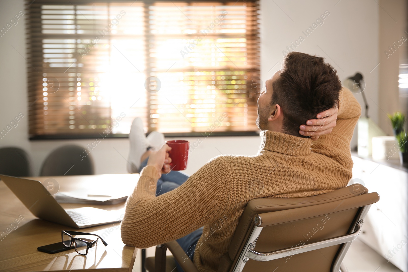 Photo of Young man with cup of drink relaxing at workplace