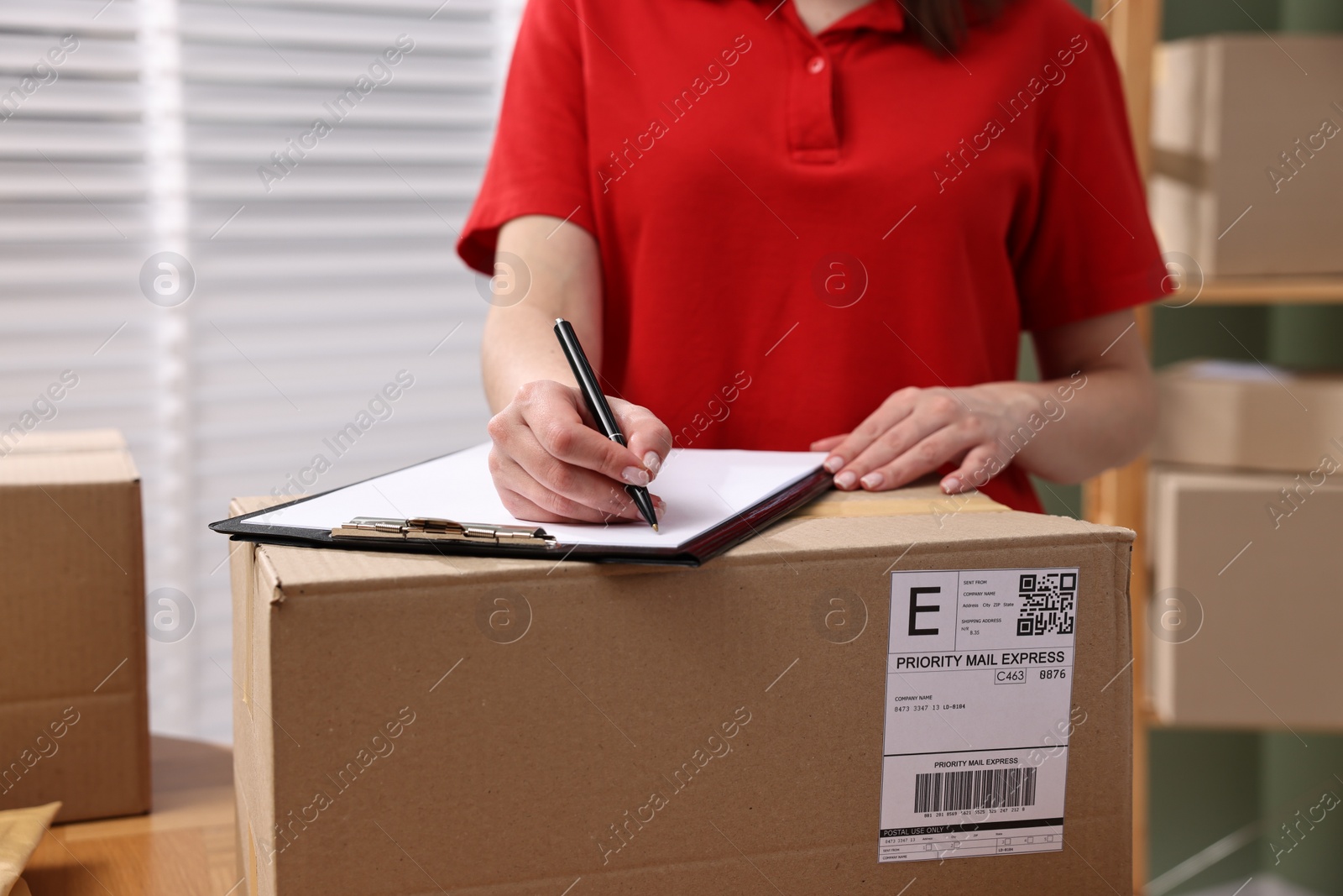 Photo of Parcel packing. Post office worker with clipboard and box indoors, closeup