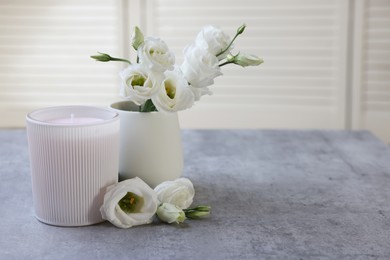 Photo of Scented candle and vase with eustoma flowers on gray marble table, space for text