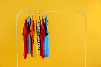 Rack with stylish children clothes on yellow background
