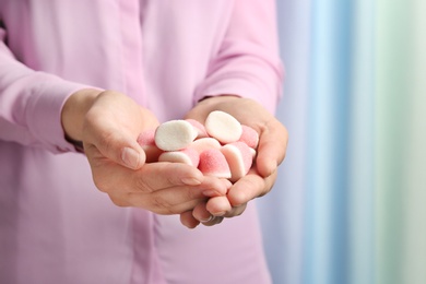 Young woman holding handful of tasty jelly candies on blurred background, closeup. Space for text