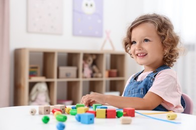 Motor skills development. Little girl playing with wooden pieces and string for threading activity at table indoors