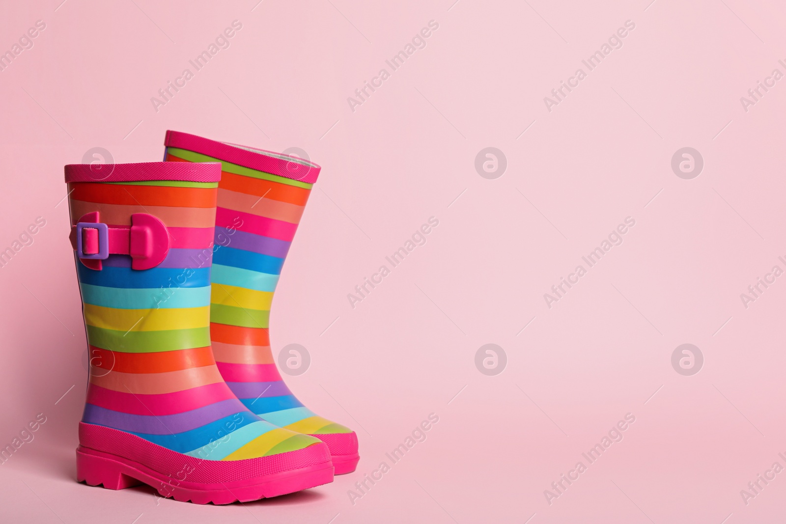 Photo of Pair of striped rubber boots on pink background. Space for text