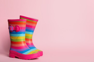 Photo of Pair of striped rubber boots on pink background. Space for text