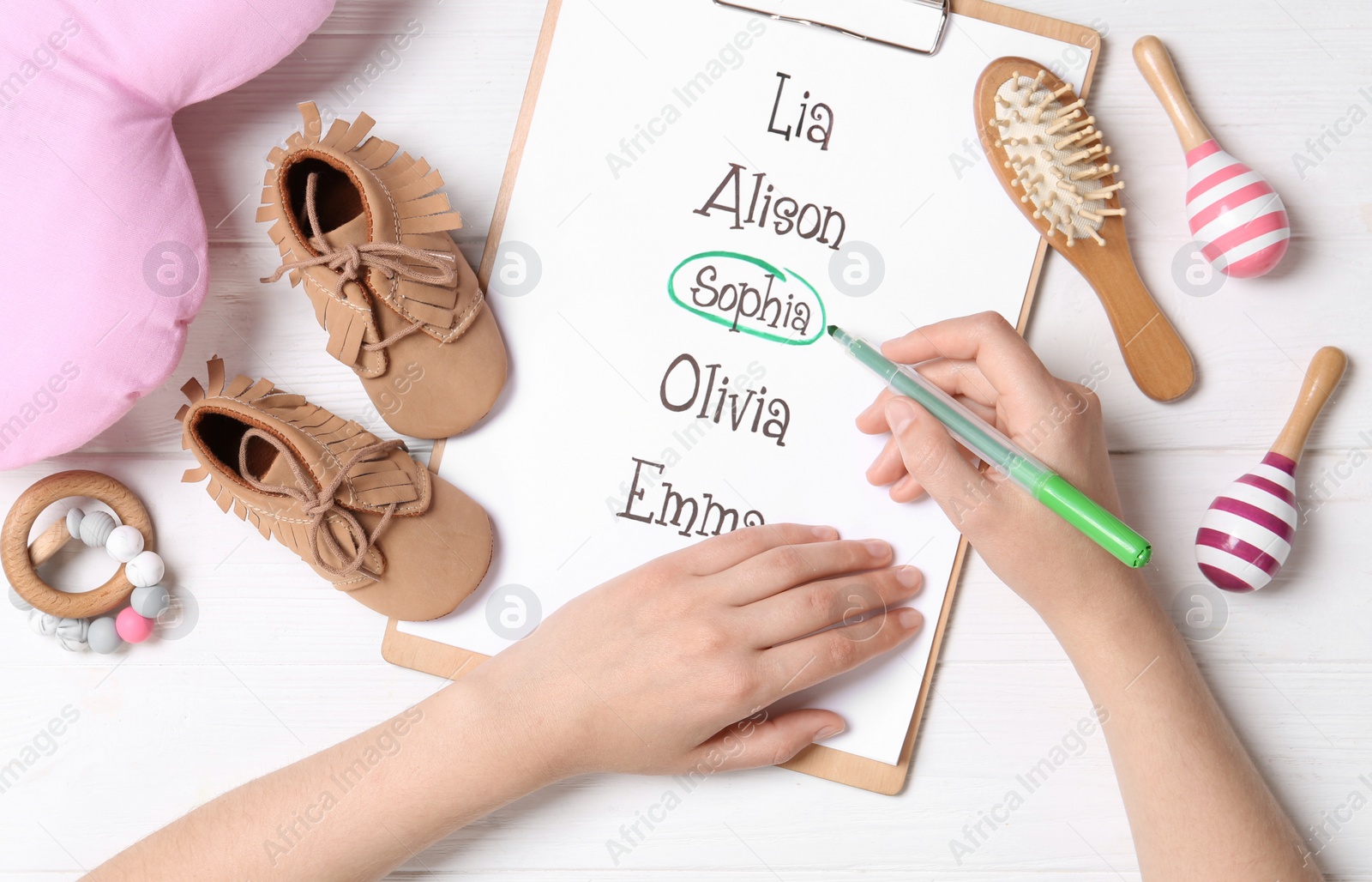 Photo of Woman marking baby name at white wooden table, top view