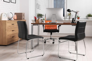 Photo of Stylish director's workplace with comfortable desk, computer and chairs for visitors in office. Interior design