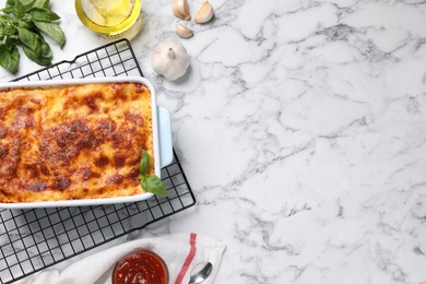 Tasty cooked lasagna in baking dish on white marble table, flat lay. Space for text