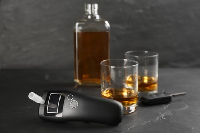 Photo of Modern breathalyzer, car key and alcohol on black table