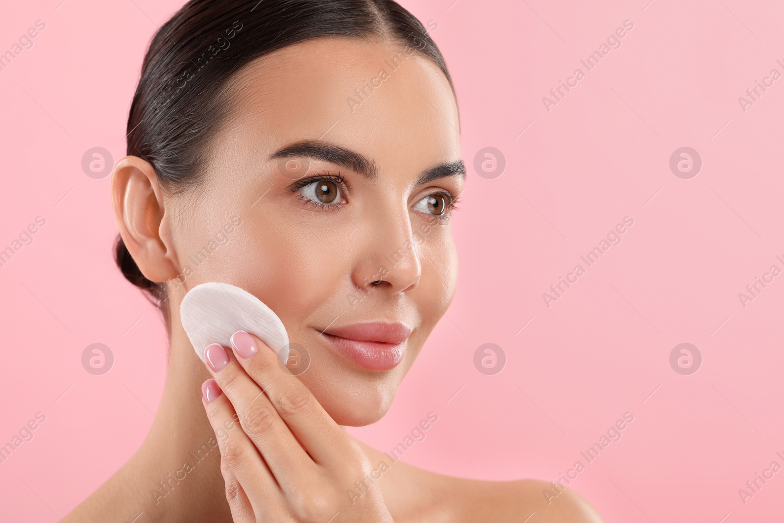 Photo of Beautiful woman removing makeup with cotton pad on pink background. Space for text