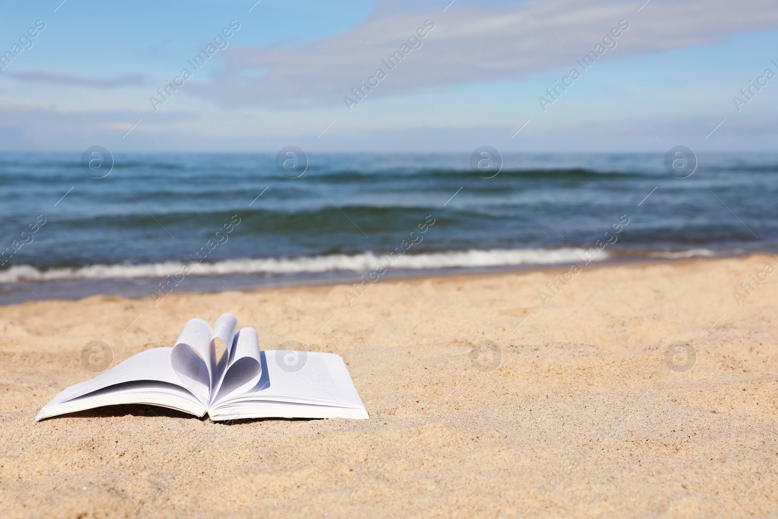 Photo of Open book on sandy beach near sea. Space for text