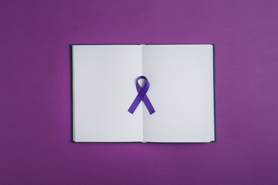 Purple awareness ribbon and open notebook on color background, top view