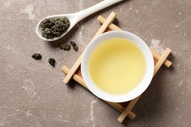 Cup of Tie Guan Yin oolong and spoon with tea leaves on color background, top view