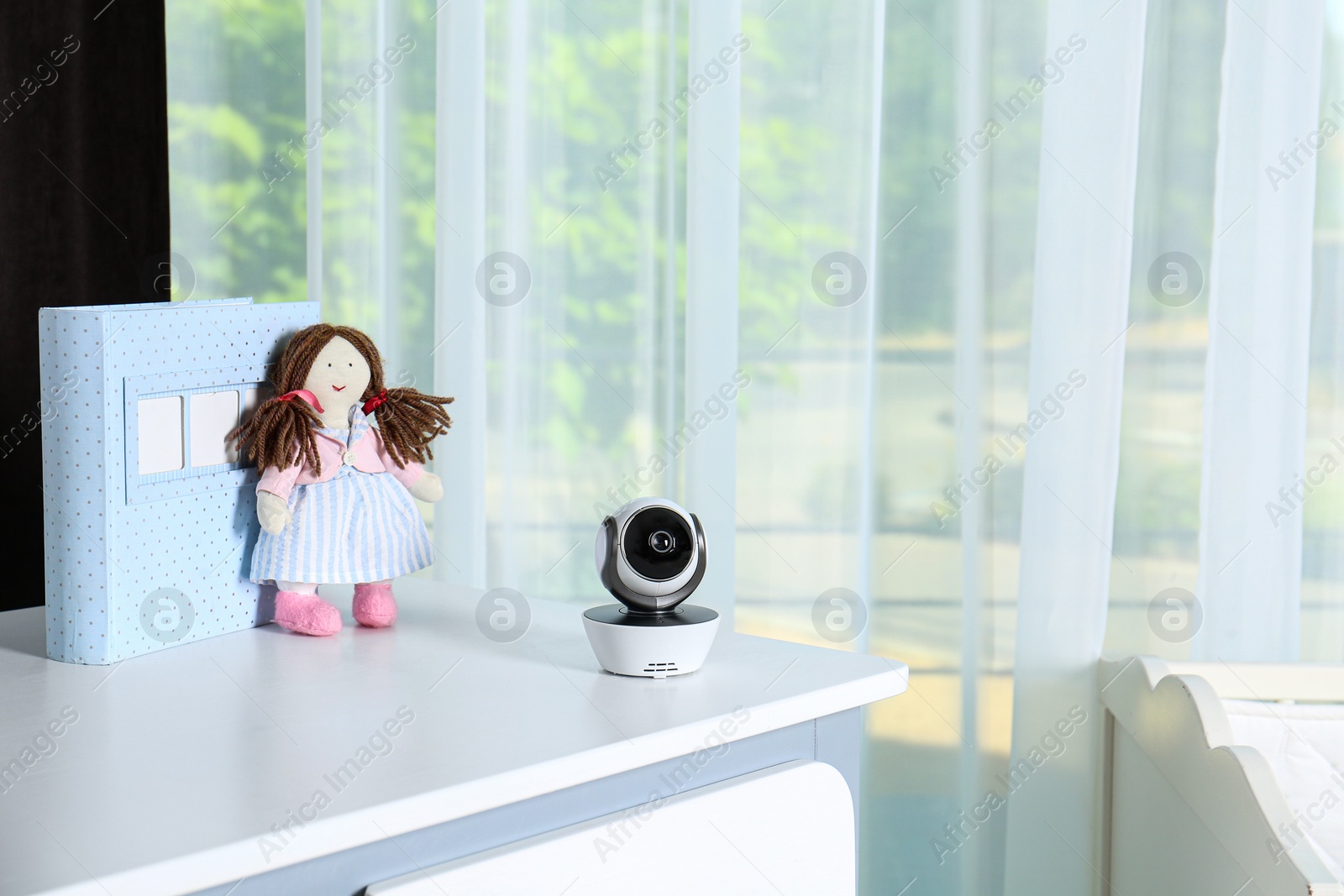 Photo of Baby camera with toy and photo album on chest of drawers in room, space for text. Video nanny