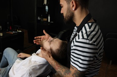 Photo of Hairdresser applying oil onto client's beard in barbershop. Professional shaving service