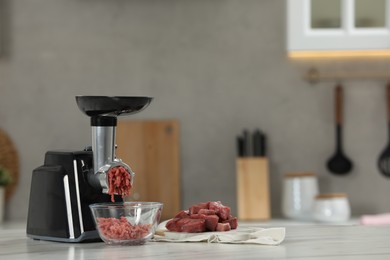Photo of Electric meat grinder with beef mince on white table in kitchen, space for text