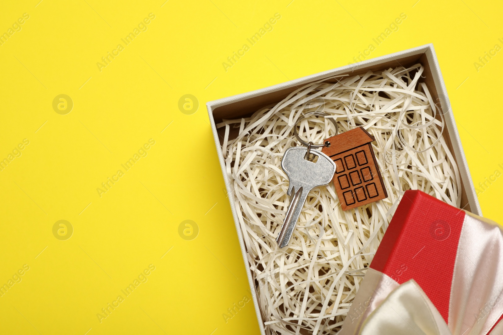 Photo of Key with trinket in shape of house on yellow background, top view and space for text. Housewarming party