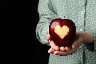 Photo of Woman holding red apple with carved heart on black background, closeup. Space for text