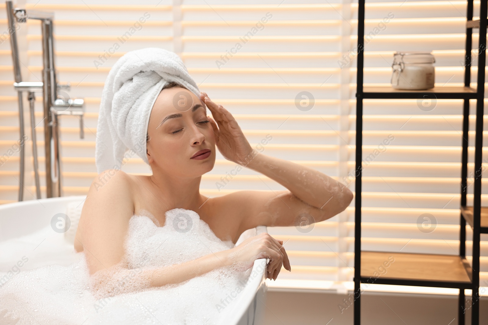 Photo of Beautiful woman taking bath with foam in tub indoors