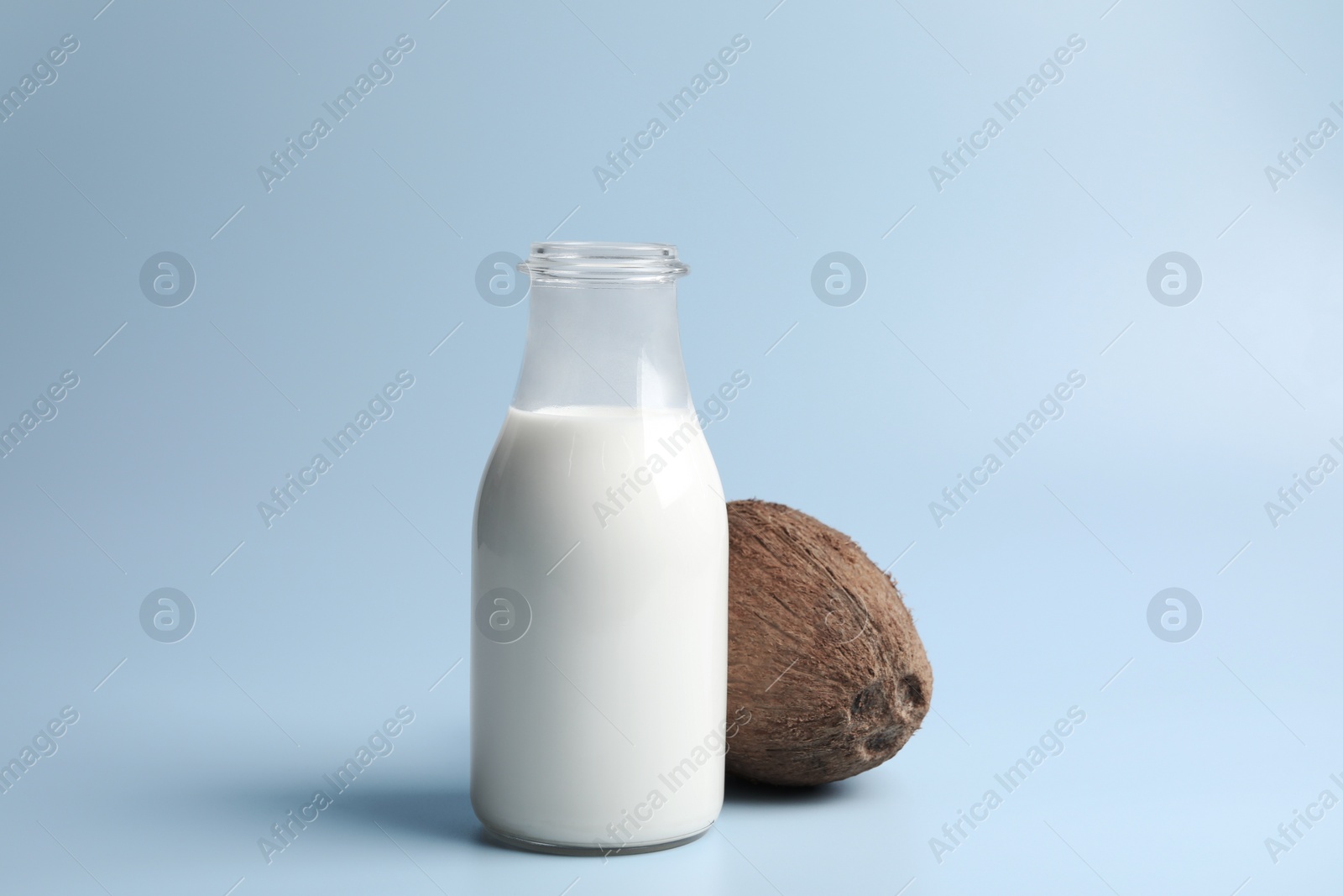 Photo of Glass bottle of delicious vegan milk and coconut on light blue background