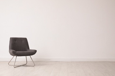 Stylish comfortable chair near white wall, space for text. Interior design