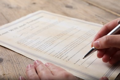 Photo of Woman signing Last Will and Testament at wooden table, closeup