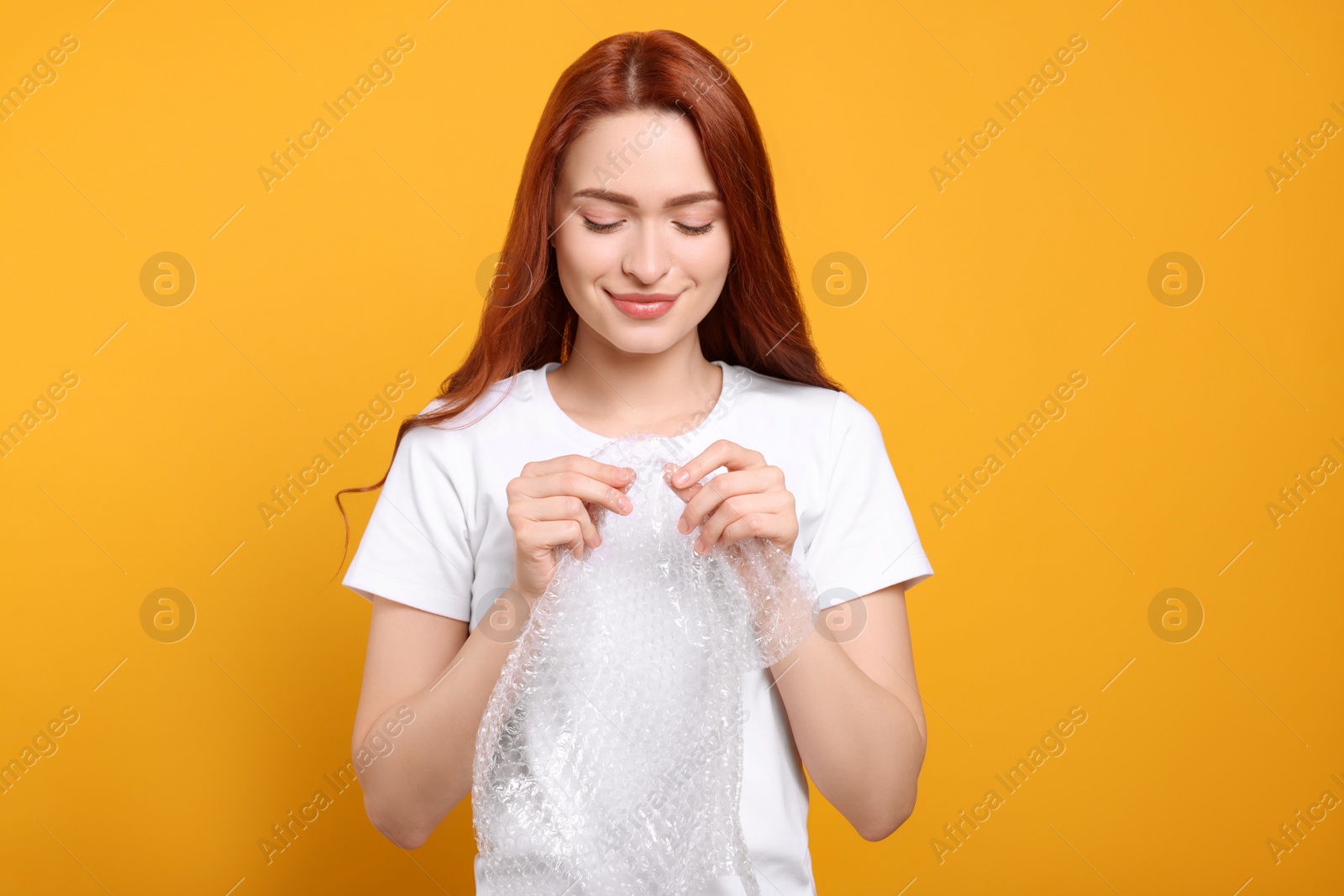 Photo of Woman popping bubble wrap on yellow background. Stress relief