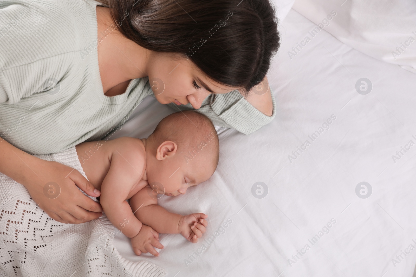 Photo of Young mother resting near her sleeping baby on bed, top view. Space for text