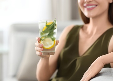 Young woman with lemonade at home, closeup. Refreshing drink