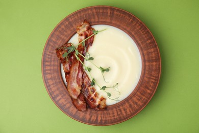 Delicious potato soup with bacon and microgreens in bowl on green table, top view