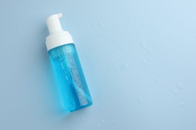 Bottle of cosmetic product on wet light blue background, top view. Space for text