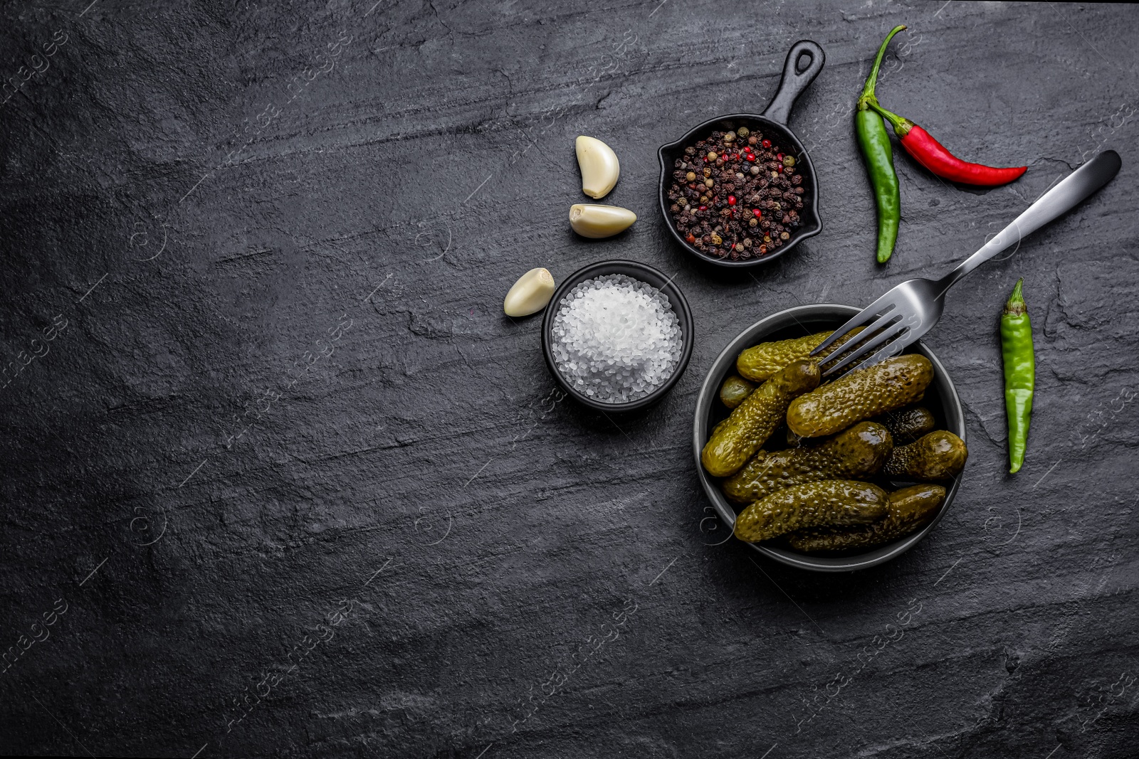 Photo of Bowl of pickled cucumbers and ingredients on black table, flat lay. Space for text