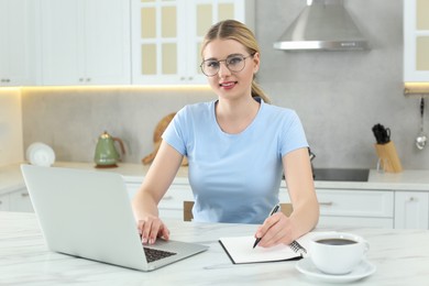 Photo of Home workplace. Happy woman working on laptop at marble desk in kitchen