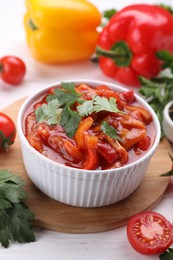 Photo of Delicious lecho in bowl and fresh ingredients on white wooden table, closeup