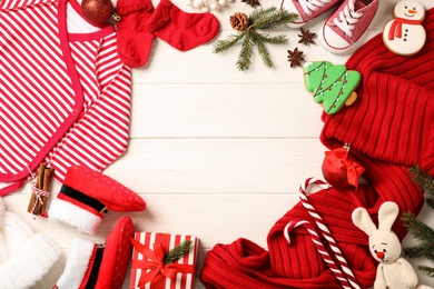 Flat lay composition with cute Christmas baby clothes on white wooden background. Space for text