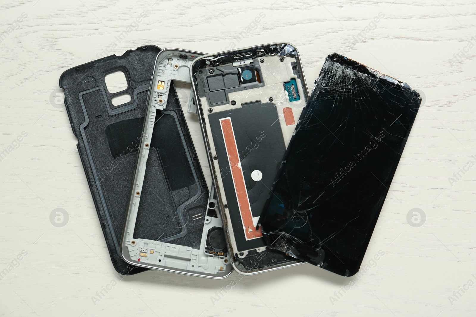 Photo of Parts of damaged smartphone on light beige wooden table, flat lay. Device repair