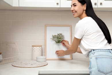 Photo of Happy woman with flowers and silicone vase attached to picture frame's glass on countertop in kitchen