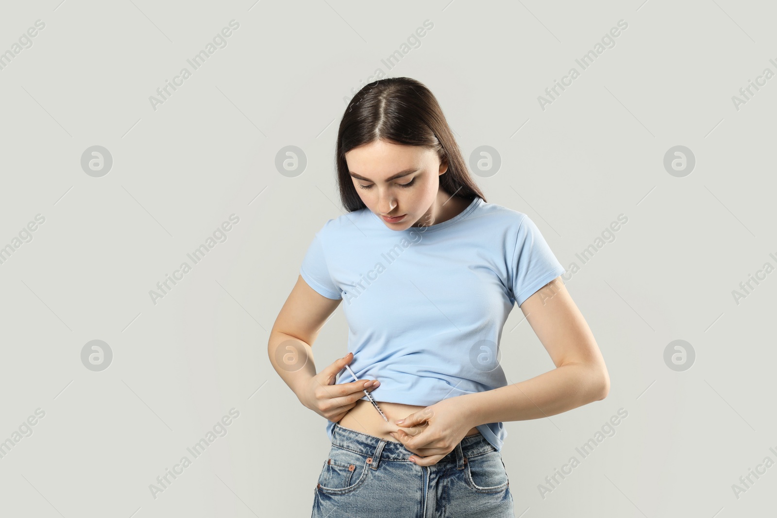 Photo of Diabetes. Woman making insulin injection into her belly on grey background