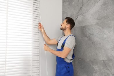 Photo of Worker in uniform opening or closing horizontal window blind indoors
