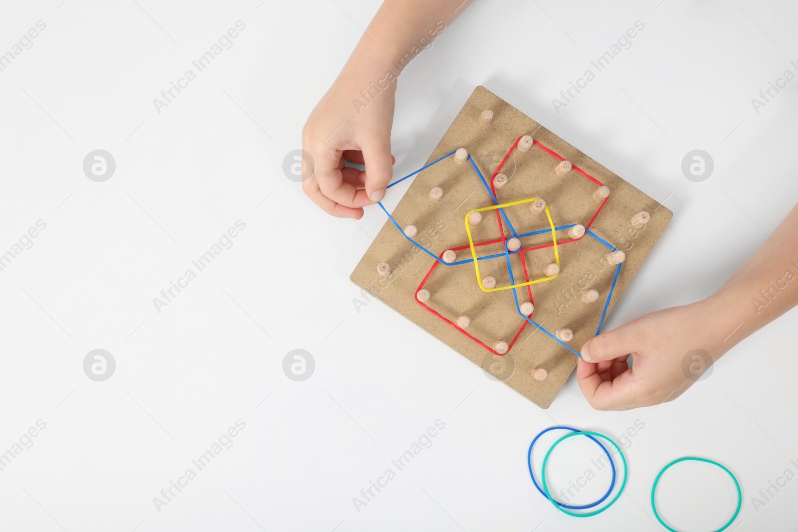 Photo of Motor skills development. Girl playing with geoboard and rubber bands at white table, top view. Space for text