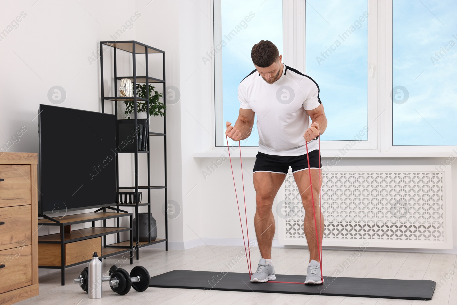 Photo of Athletic man doing exercise with elastic resistance band on mat at home