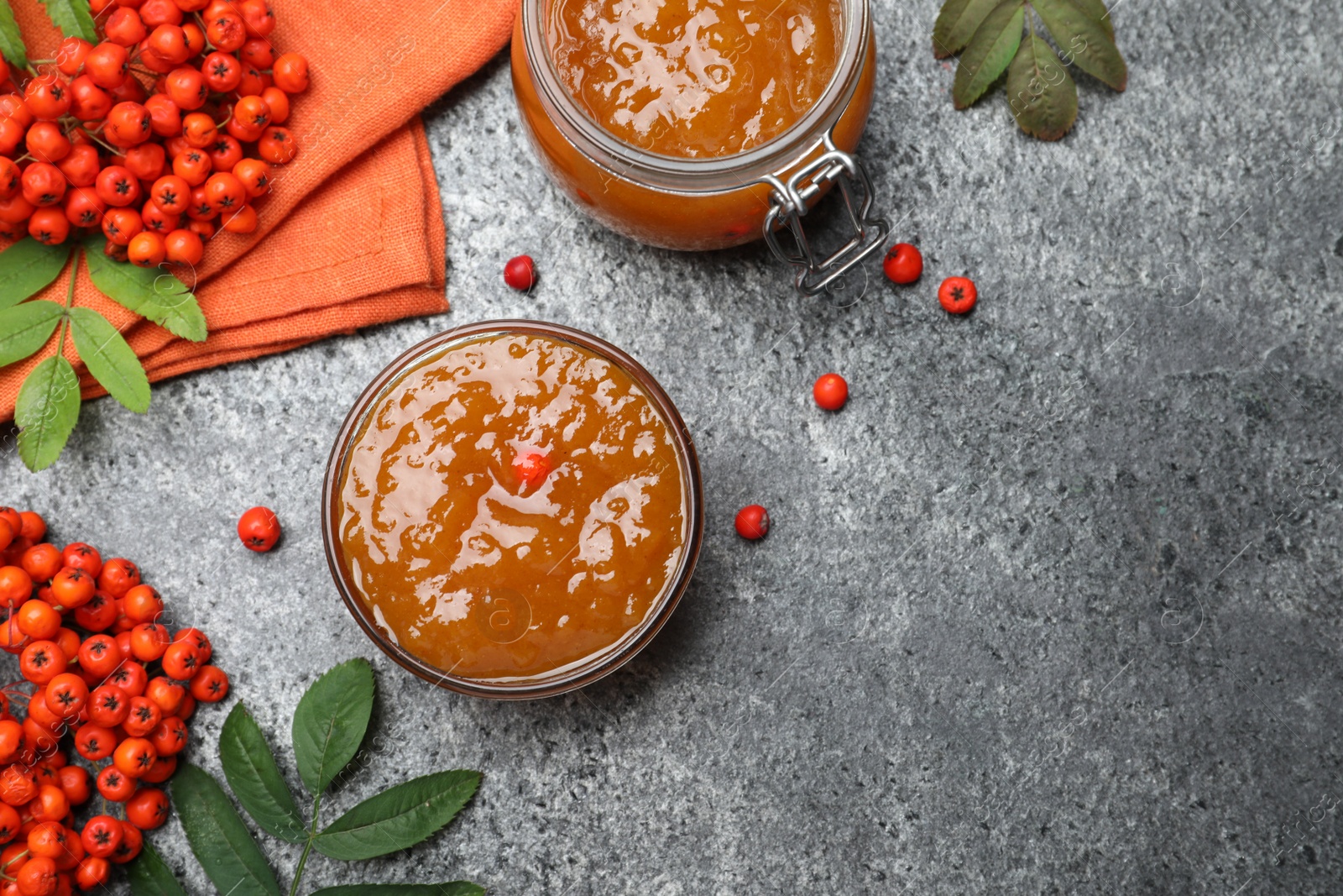 Photo of Flat lay composition with delicious rowan jam and berries on grey table. Space for text