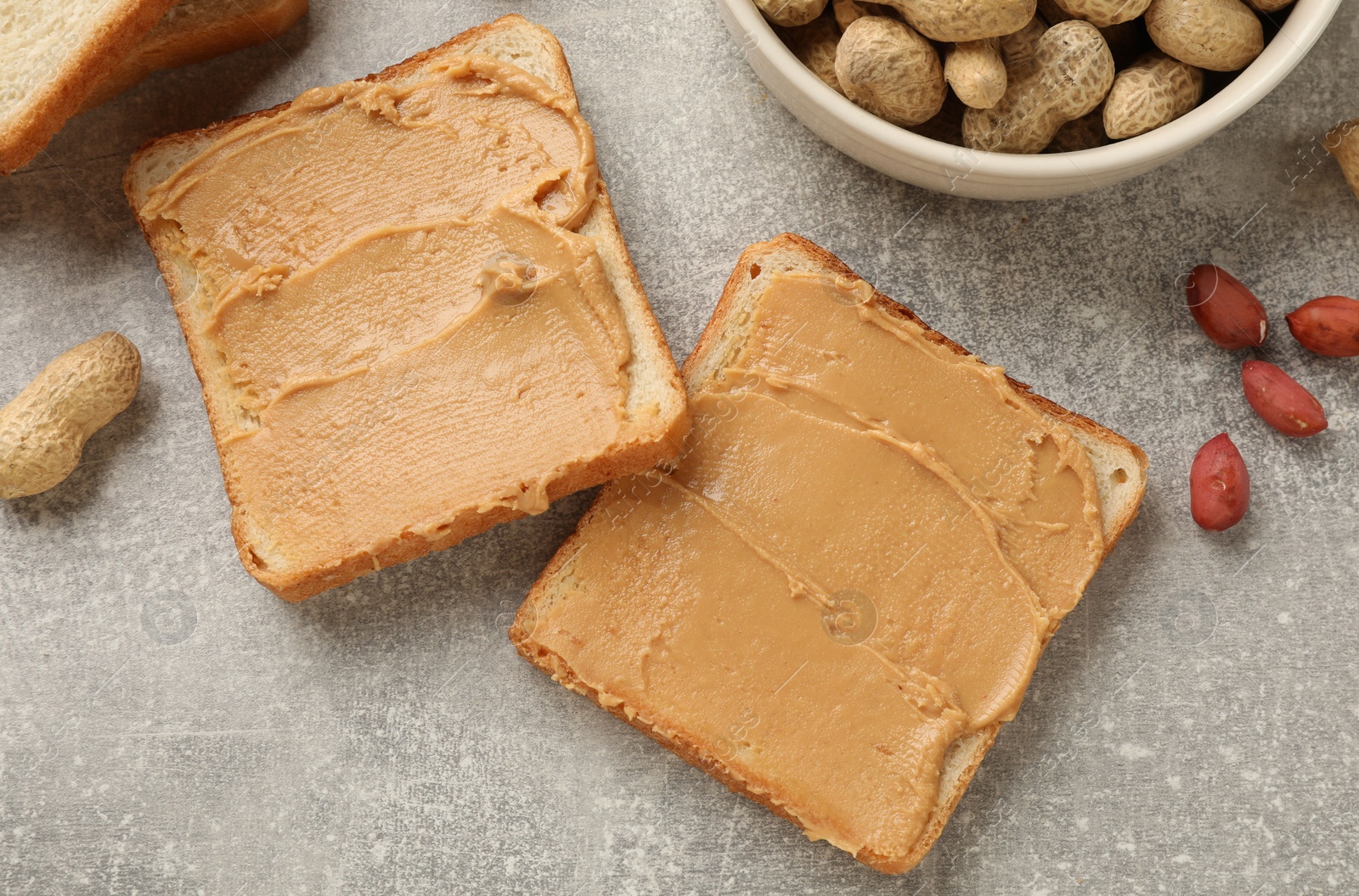 Photo of Tasty peanut butter sandwiches and peanuts on gray table, flat lay