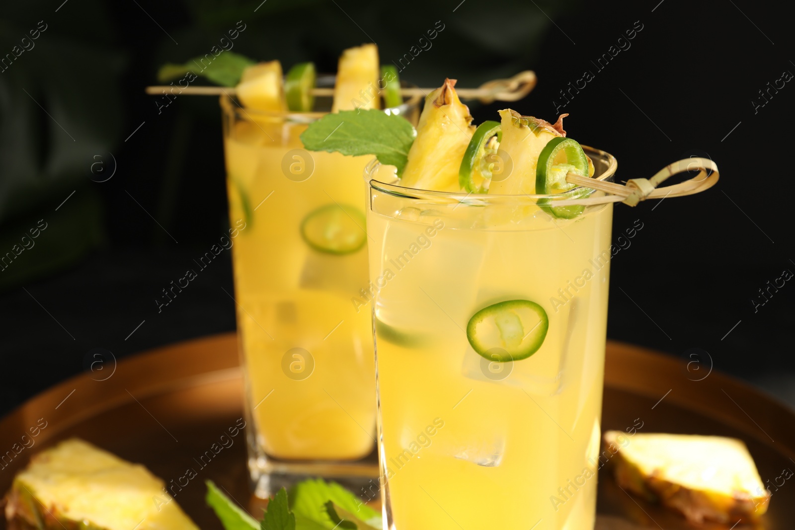 Photo of Glasses of tasty pineapple cocktail with sliced fruit, mint and chili pepper on tray, closeup