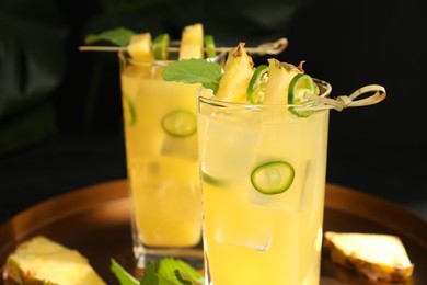 Photo of Glasses of tasty pineapple cocktail with sliced fruit, mint and chili pepper on tray, closeup