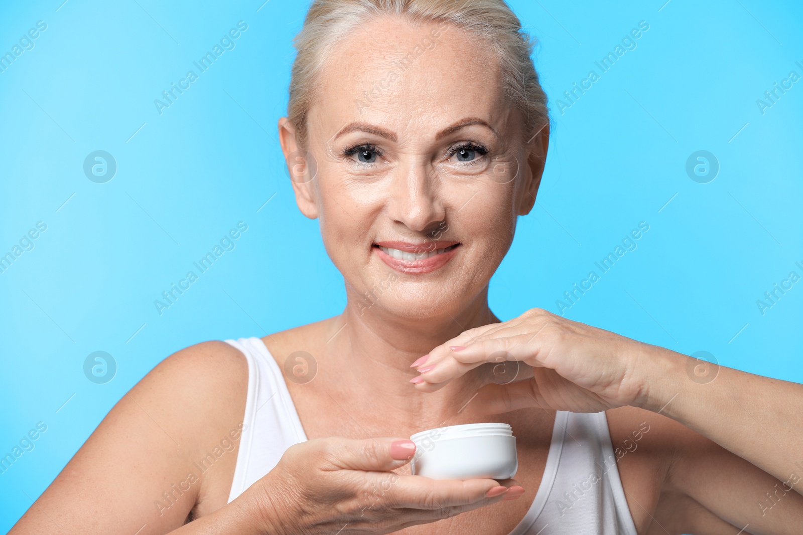 Photo of Portrait of beautiful mature woman with perfect skin holding jar of cream on light blue background