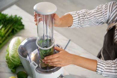 Young woman making tasty fresh juice at table in kitchen, closeup