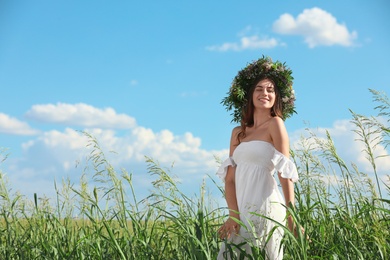 Photo of Young woman wearing wreath made of beautiful flowers in field on sunny day